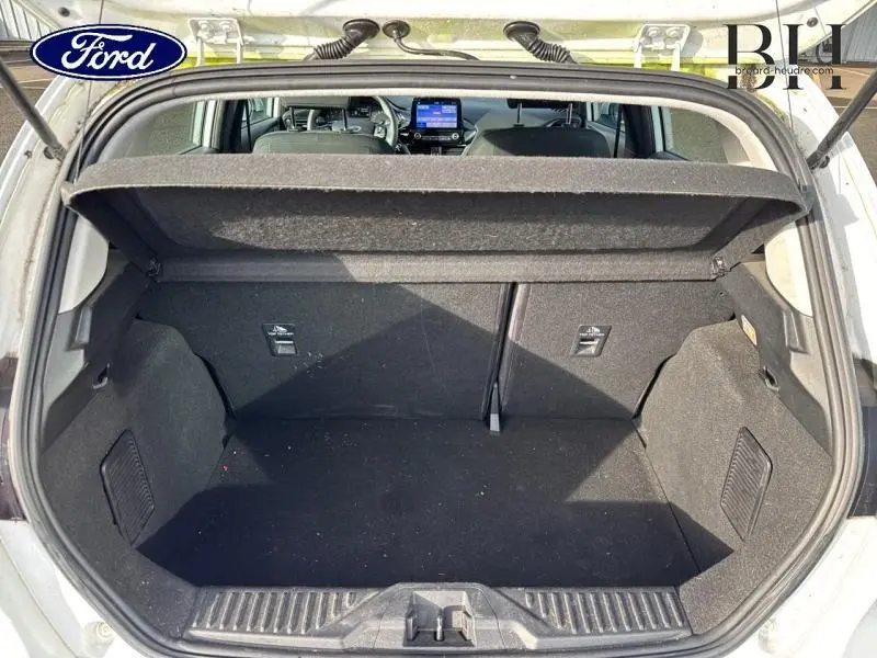 Vue sur le coffre ouvert d'une Ford Fiesta blanc glacier, montrant l'intérieur spacieux et la tablette arrière relevée.