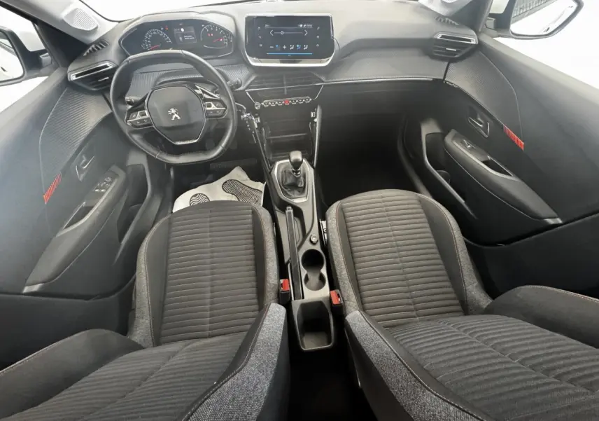 Vue intérieure avant de la Peugeot 208 2020, tableau de bord noir avec écran tactile central et sièges tissu gris.