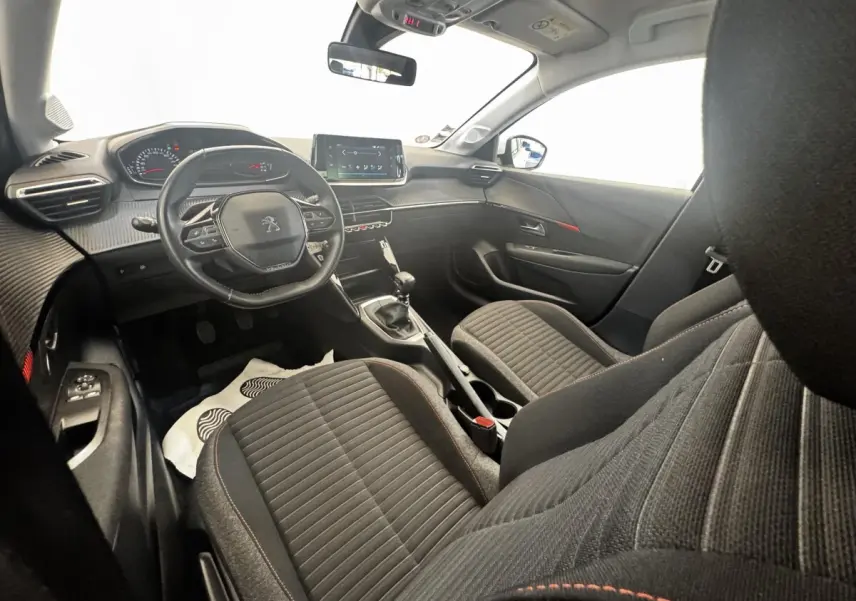 Vue intérieure côté conducteur de la Peugeot 208 blanche, montrant le tableau de bord et la console centrale avec écran tactile.