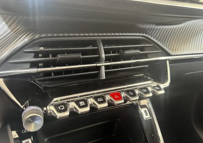 Gros plan sur la console centrale noire brillante de la Peugeot 208 2020 avec boutons chromés et finition carbone.