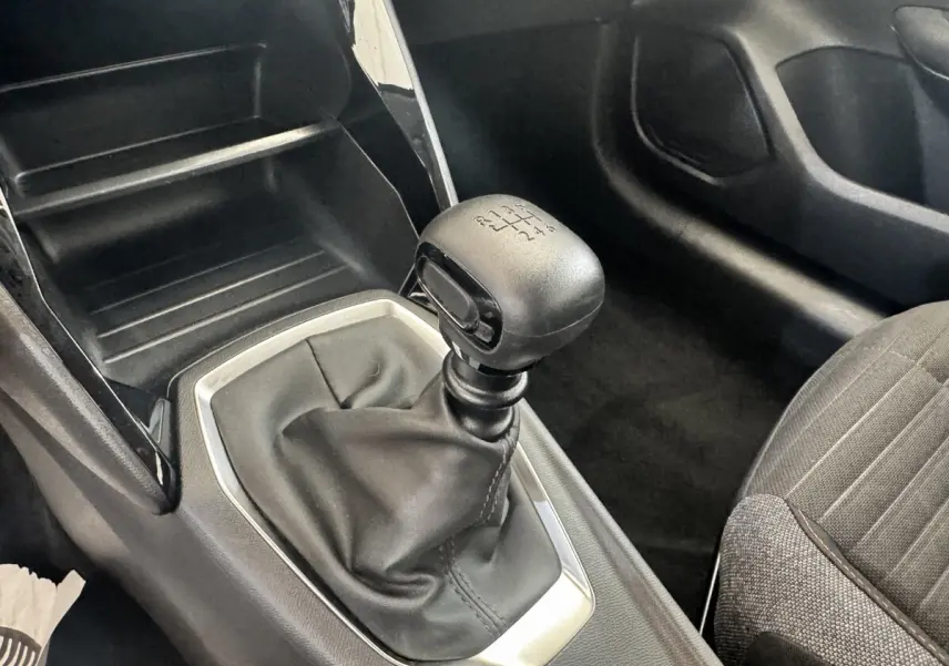 Gros plan sur le levier de vitesses manuel noir de la Peugeot 208 PureTech 100, intérieur avec sellerie grise.