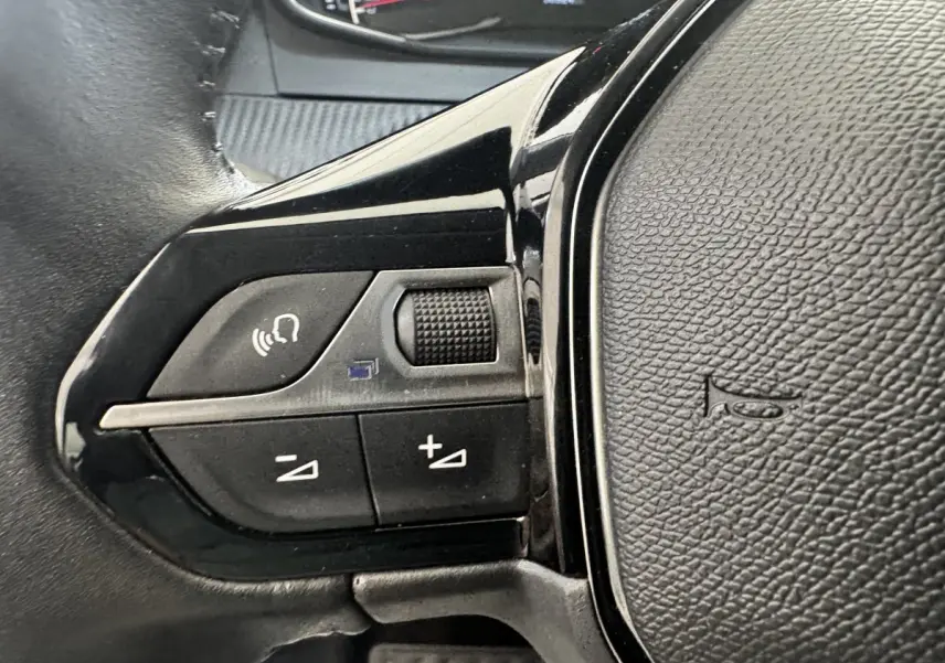 Gros plan sur les commandes vocales et volume du volant cuir noir de la Peugeot 208 PureTech 100 S&S Active Business.
