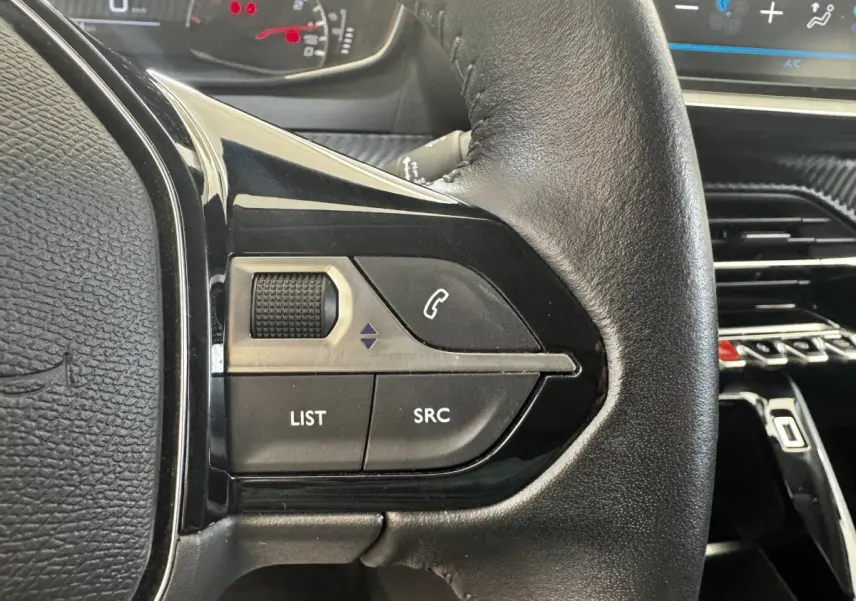 Gros plan sur le volant cuir noir de la Peugeot 208 blanc, avec commandes audio et téléphone intégrées.