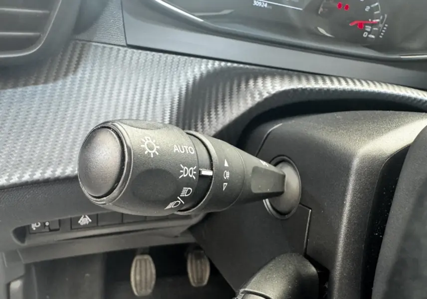 Gros plan sur la commande des phares à gauche du volant dans l’habitacle noir de la Peugeot 208 blanche de 2020.