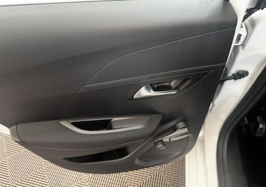 Vue intérieure de la porte arrière droite noire d’une Peugeot 208 blanche, poignée et manivelle de vitre visibles.