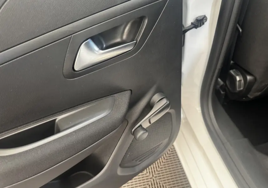 Vue rapprochée de la porte arrière gauche noire d'une Peugeot 208 blanche, avec manivelle de vitre manuelle visible.
