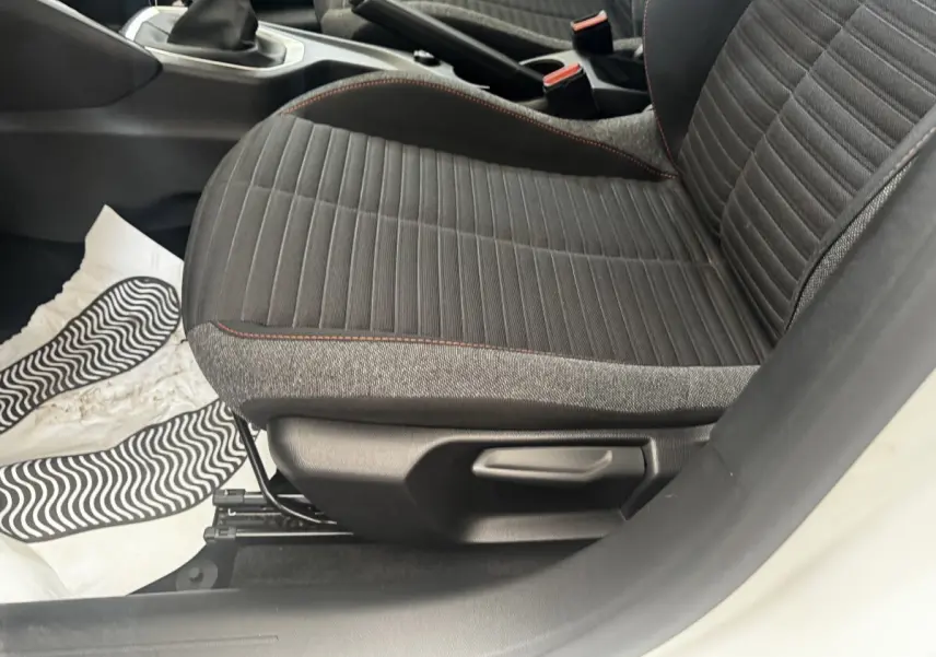 Gros plan sur le siège avant droit noir avec surpiqûres rouges d’une Peugeot 208 blanche, intérieur visible côté conducteur.