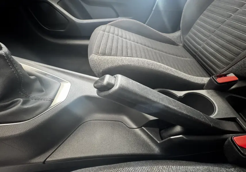 Vue rapprochée de la console centrale avec frein à main levé et siège tissu gris à motifs dans une Peugeot 208 blanche.
