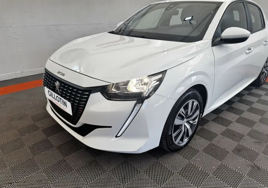 Peugeot 208 blanc vue 3/4 avant droit, avec calandre noire distinctive et feux allumés dans un showroom.