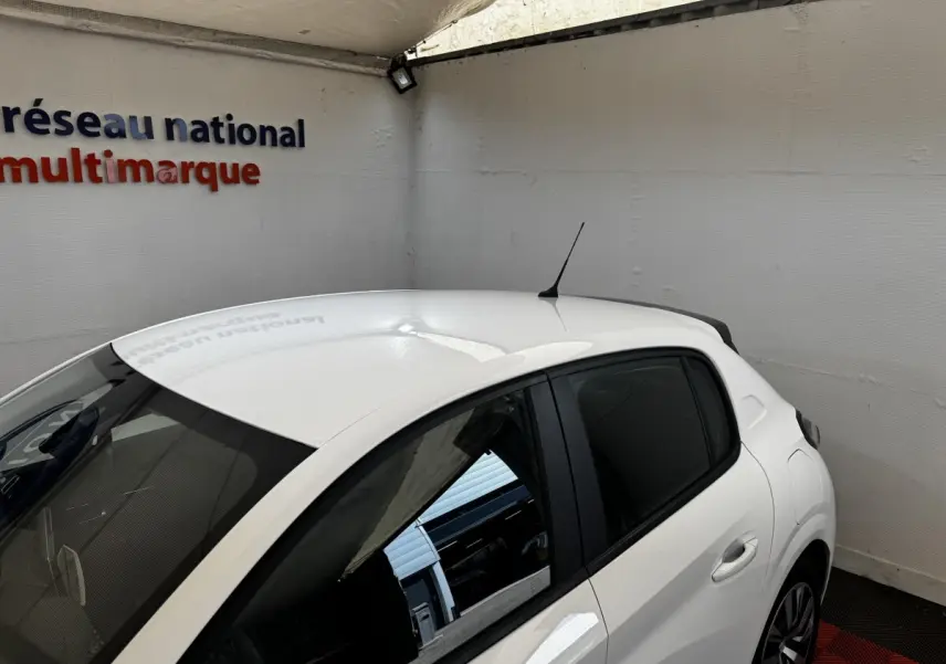 Vue 3/4 arrière droite d'une Peugeot 208 blanche 2020 garée en intérieur avec vitres teintées et antenne de toit.