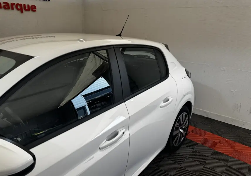 Vue côté droit arrière d'une Peugeot 208 blanche garée sur un sol à damiers noir et rouge, en intérieur.