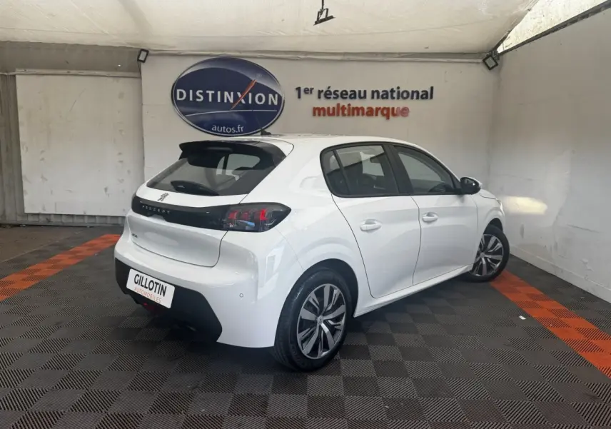 Peugeot 208 blanc vue 3/4 arrière droit en intérieur, avec jantes alliage et bande noire distinctive sur la porte.