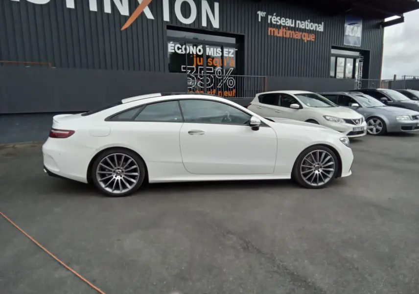 Profil côté gauche d'une Mercedes Classe E Coupé blanche AMG Line 220D 2020 avec jantes alliage et toit panoramique.