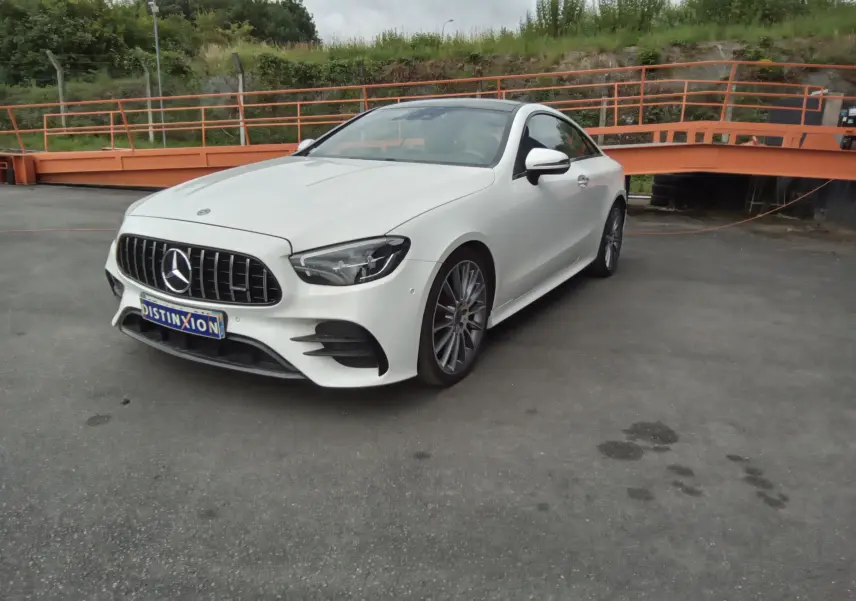 Mercedes Classe E Coupé 220D AMG Line blanc en 3/4 avant droit, avec calandre distinctive et jantes alliage 19 pouces.
