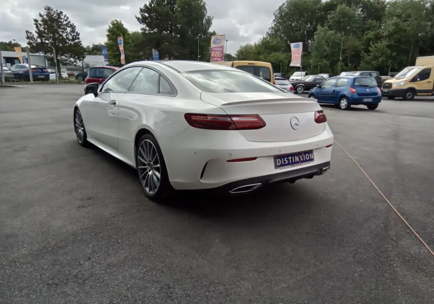 Vue 3/4 arrière gauche d'une Mercedes Classe E Coupé blanche AMG Line avec jantes alliage et feux LED distinctifs.