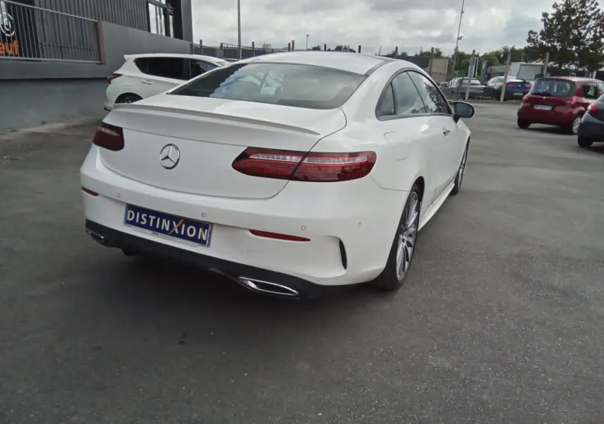 Vue 3/4 arrière droite d'une Mercedes Classe E Coupé 220D blanche avec finition AMG Line et feux arrière LED distinctifs.