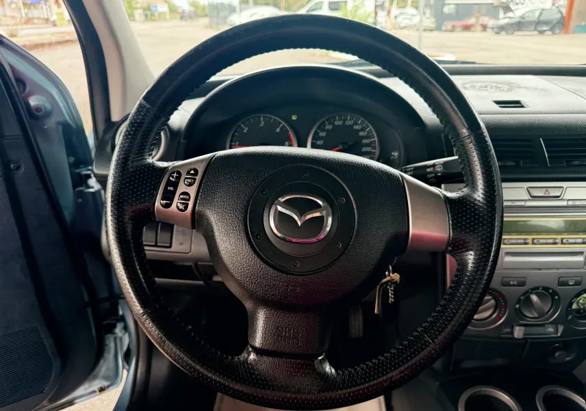 Volant en cuir noir avec logo Mazda au centre, tableau de bord et console centrale d'une Mazda2 gris vue de l'intérieur côté conducteur.