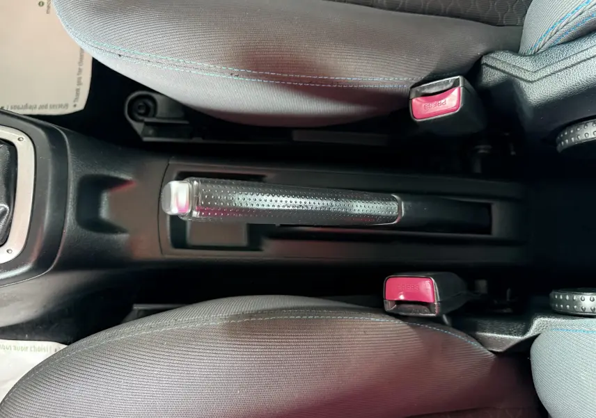 Vue rapprochée de la console centrale de la Mazda2 2004 montrant le frein à main et les ceintures de sécurité avec boutons rouges.