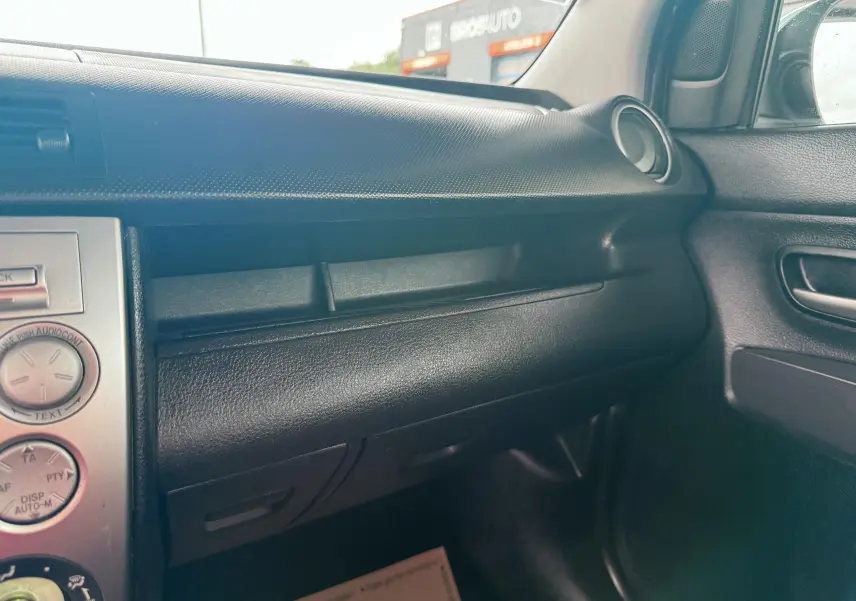 Vue intérieure côté passager du tableau de bord noir de la Mazda2 gris 2004 avec détails de la console centrale et portière.