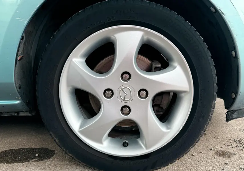 Gros plan sur la roue arrière droite d'une Mazda2 gris clair, montrant l'aile et le passage de roue.