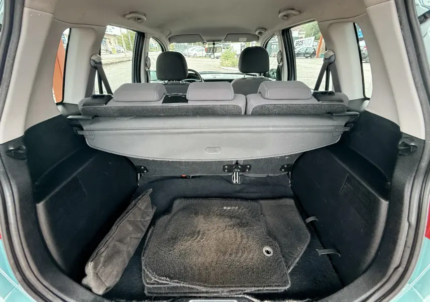 Coffre ouvert d'une Mazda2 gris, vue de l'arrière montrant le tapis de sol et la plage arrière en tissu noir.