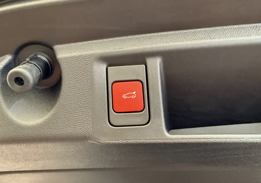 Gros plan sur le bouton rouge d'ouverture électrique du coffre dans l'habitacle d'une Peugeot 308 Hybrid blanche.