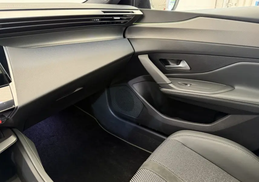 Vue intérieure côté passager de la Peugeot 308 Hybrid 136 e-DCS6 GT 2024 avec sellerie grise et tableau de bord noir.