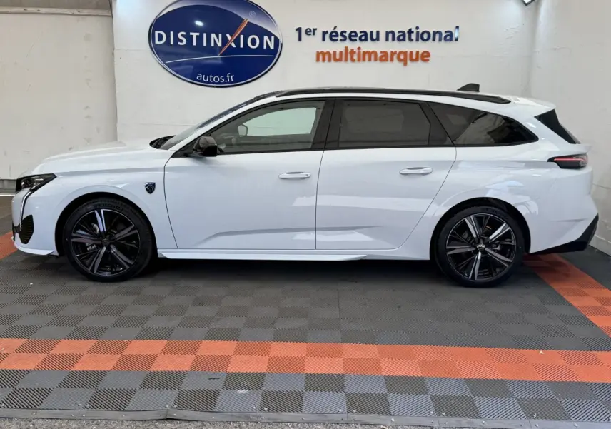 Profil côté gauche d'une Peugeot 308 Hybrid 136 e-DCS6 GT blanche avec jantes noires et toit ouvrant panoramique.