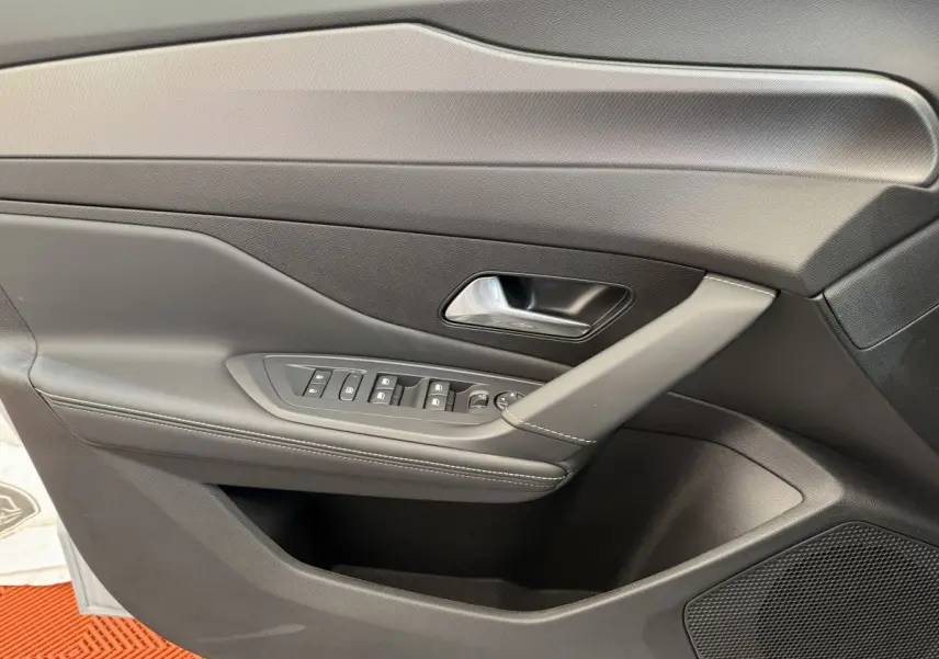 Vue rapprochée de la porte intérieure côté gauche de la Peugeot 308 Hybrid 136 e-DCS6 GT 2024 avec commandes et poignée grises.