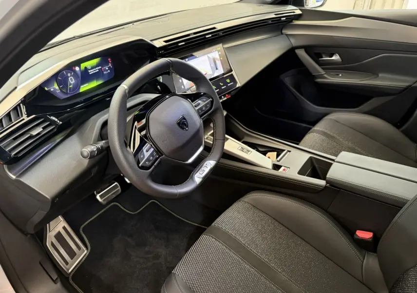 Intérieur noir de la Peugeot 308 Hybrid 136 GT vu côté conducteur, avec tableau de bord digital et volant cuir GT.