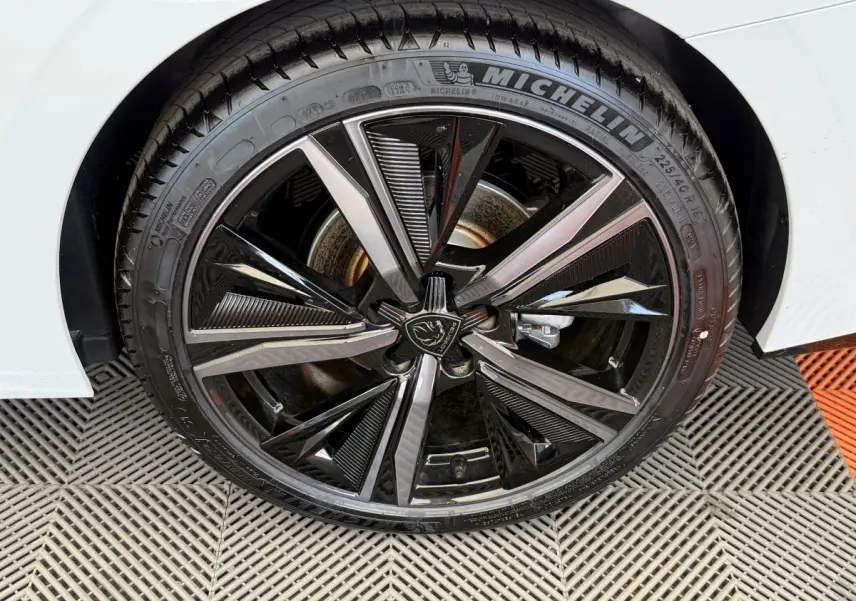 Gros plan sur la roue avant droite blanche d'une Peugeot 308 Hybrid 136 e-DCS6 GT avec jante noire et argentée distinctive.