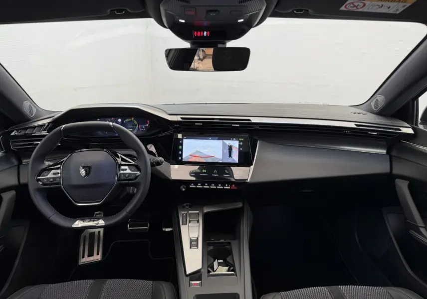 Intérieur noir de la Peugeot 308 Hybrid 136 e-DCS6 GT 2024, vue frontale sur tableau de bord et volant multifonctions.