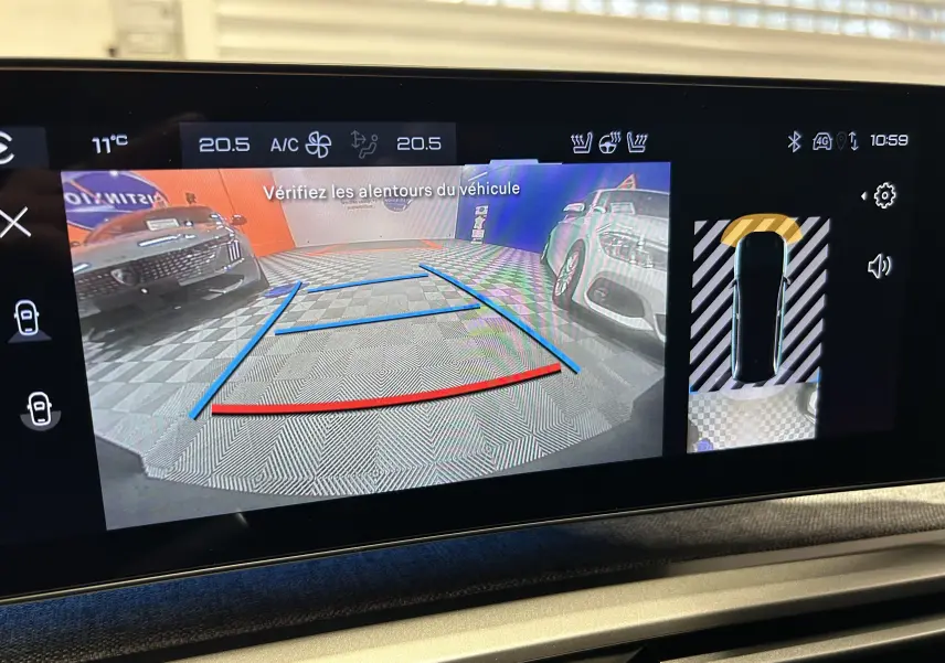 Vue caméra de recul du Peugeot 5008 bleu obsession, montrant l'arrière avec repères de guidage et véhicules stationnés.