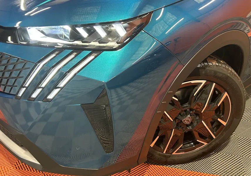 Gros plan sur l'avant droit bleu obsession du Peugeot 5008 III Hybrid 145 GT, avec feux LED et jante noire à inserts cuivrés.