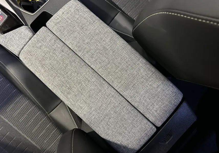 Détail de l'accoudoir central en tissu gris et cuir noir dans l'habitacle du Peugeot 5008 III Hybrid 145 GT.