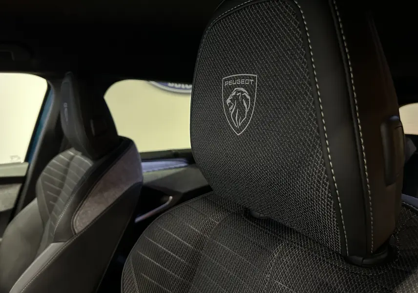 Gros plan sur l'appui-tête avant droit avec logo Peugeot, tissu noir et surpiqûres blanches dans l'habitacle du 5008 2025.