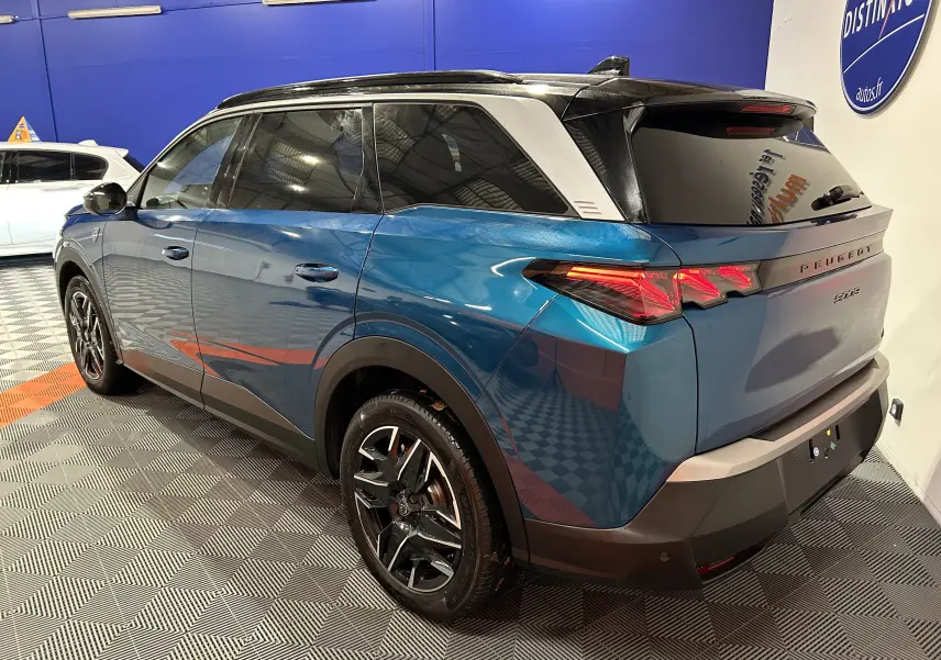 Vue 3/4 arrière droite du Peugeot 5008 hybride bleu obsession avec toit noir et feux arrière LED allumés.