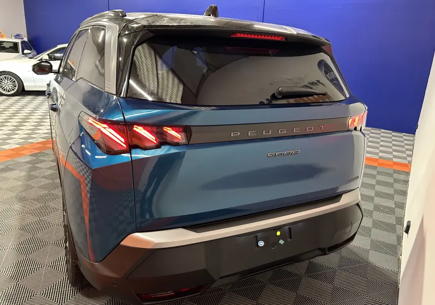 Vue 3/4 arrière droite du Peugeot 5008 bleu obsession avec feux arrière LED allumés dans un showroom.