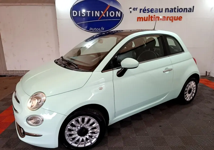 Vue 3/4 avant droite d'une Fiat 500 Lounge 2019 vert clair avec jantes alliage et phares allumés en intérieur showroom.