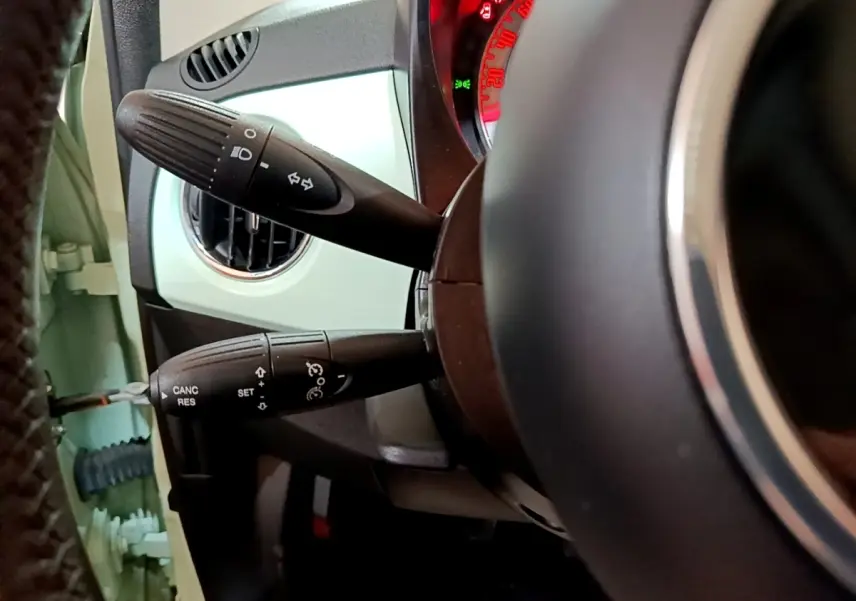 Détail des commandes au volant côté gauche d'une Fiat 500 Lounge 2019 vert clair, avec tableau de bord partiellement visible.