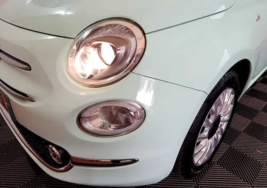 Gros plan sur l'avant droit vert clair d'une FIAT 500 1.2 8V 69ch Lounge avec phare allumé et jante alu.