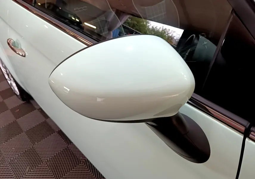 Gros plan sur le rétroviseur côté gauche blanc nacré d'une Fiat 500 Lounge 2019 avec porte assortie visible.