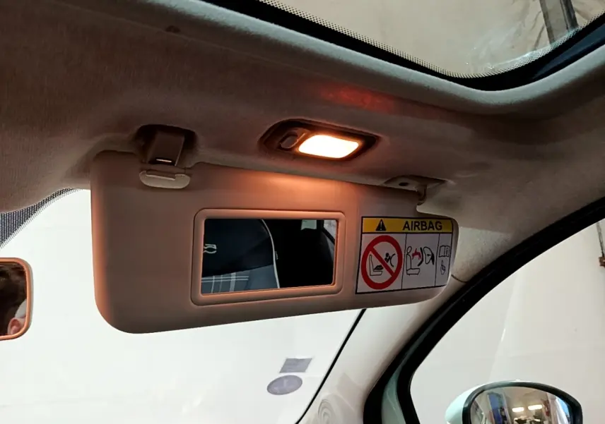 Détail du pare-soleil côté conducteur avec miroir éclairé et avertissement airbag dans l'habitacle clair d'une Fiat 500.