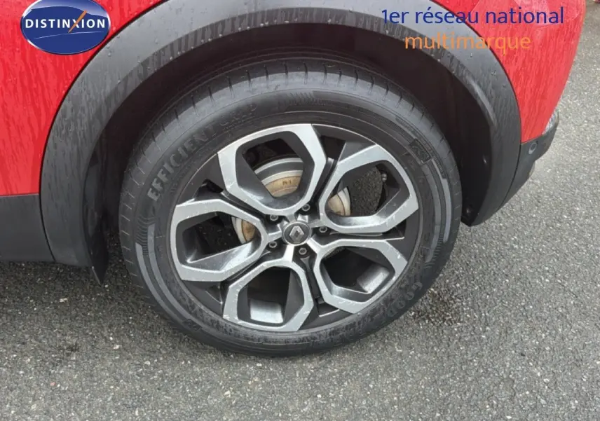 Gros plan sur la roue arrière droite d’un Renault Captur rouge flamme avec jante alliage à motifs géométriques.