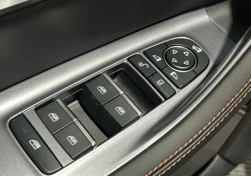 Gros plan sur les commandes de lève-vitres et rétroviseurs côté conducteur avec surpiqûres marron sur cuir noir.