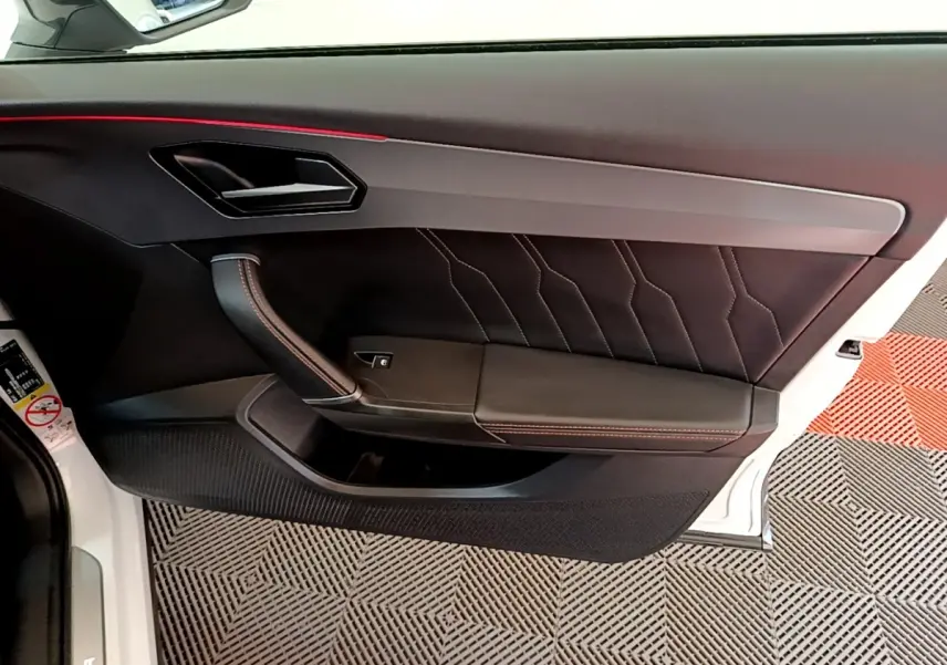Vue intérieure côté gauche de la porte avant d'une CUPRA Formentor 2023 avec garniture noire et surpiqûres rouges.