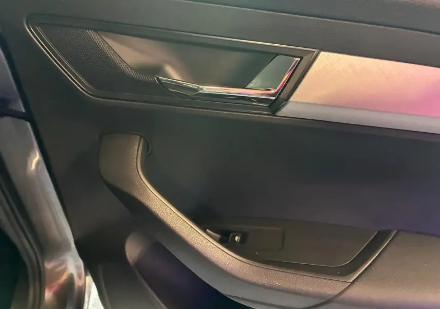 Détail de la poignée intérieure côté gauche d'une Skoda Karoq gris 2023 avec insert chromé et garniture noire.