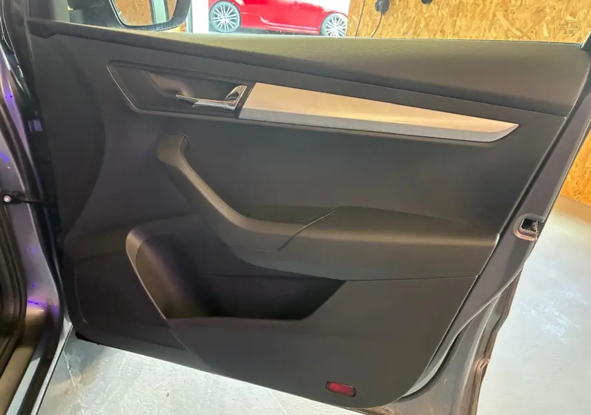 Vue intérieure de la porte avant gauche d’un Skoda Karoq gris, avec insert décoratif clair et poignée chromée.