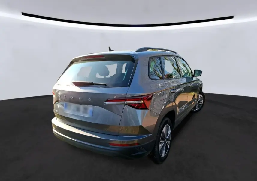 Vue 3/4 arrière droite d'un Skoda Karoq gris 2023 avec jantes alu 17 pouces et toit avec barres de pavillon noires.