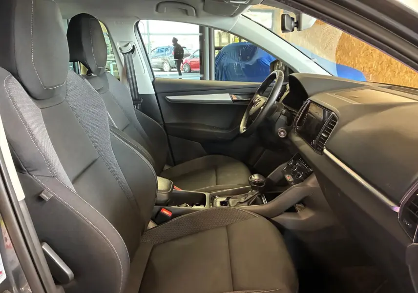 Intérieur avant du Skoda Karoq gris 2023, vue côté conducteur, sièges noirs et tableau de bord moderne.